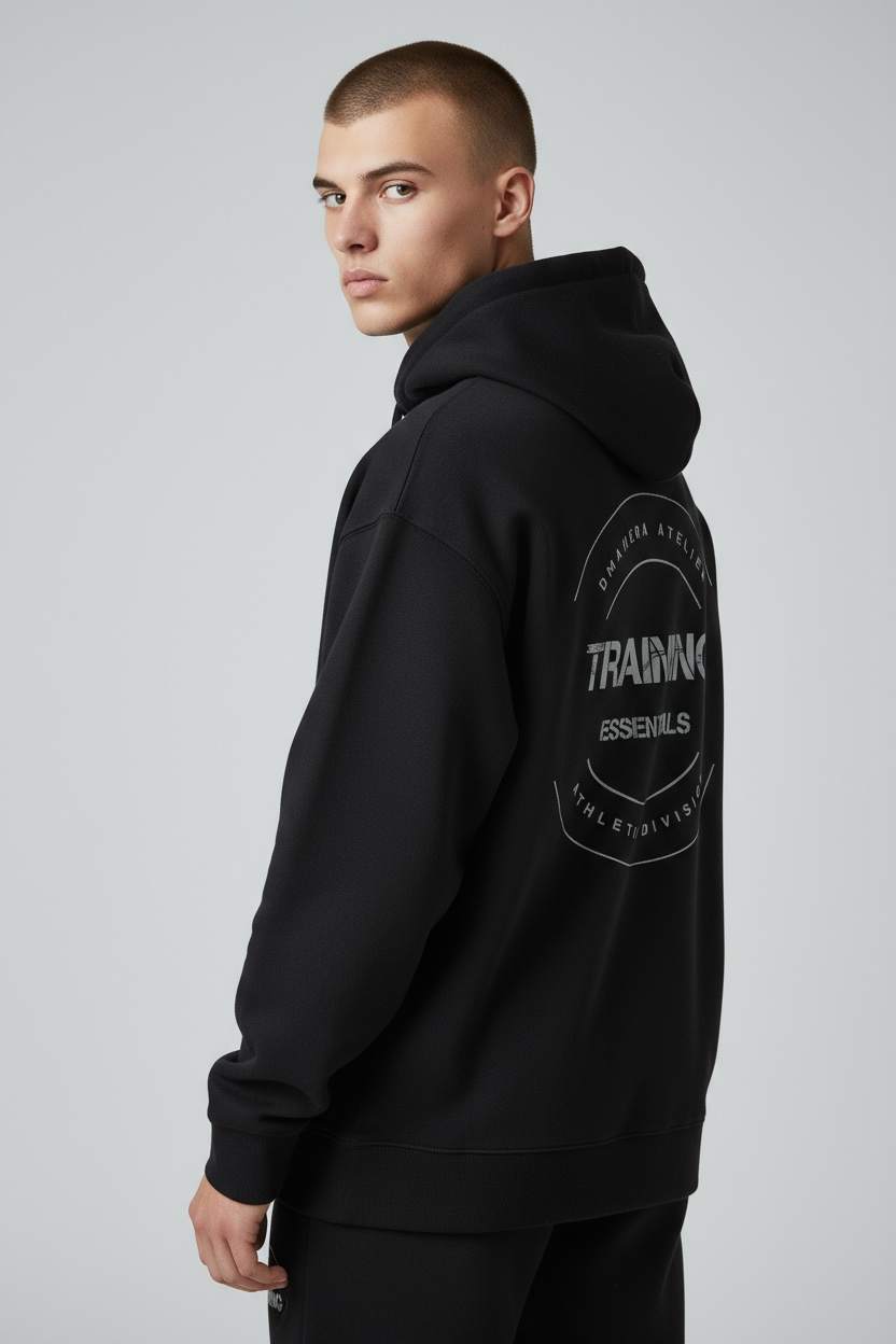 Junger Mann im schwarzen DMANERA Atelier Hoodie mit Trainings-Print, neutrales Studio-Setting.