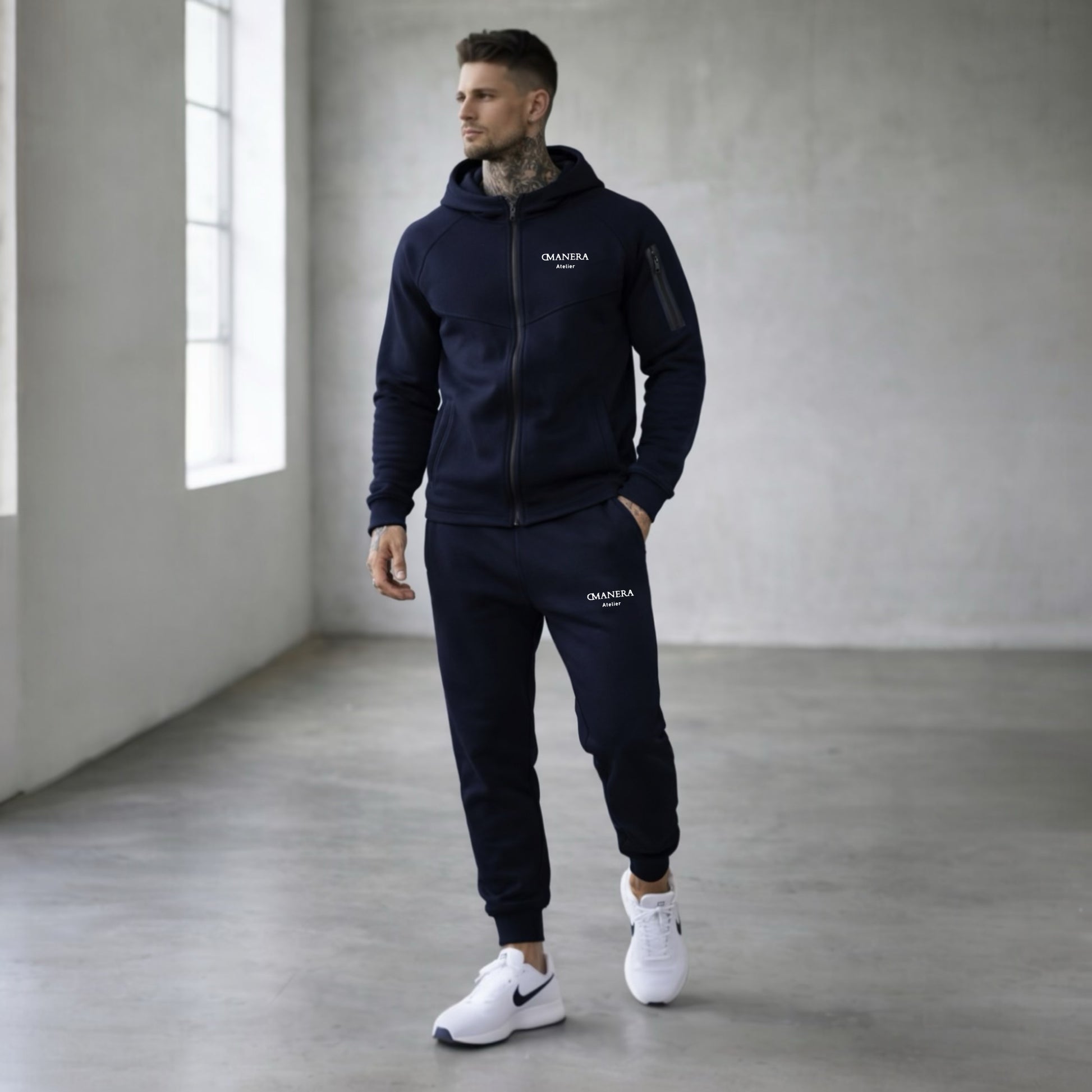 Mann trägt dunkelblauen Hoodie und Jogginghose in modernem, minimalistischen Raum